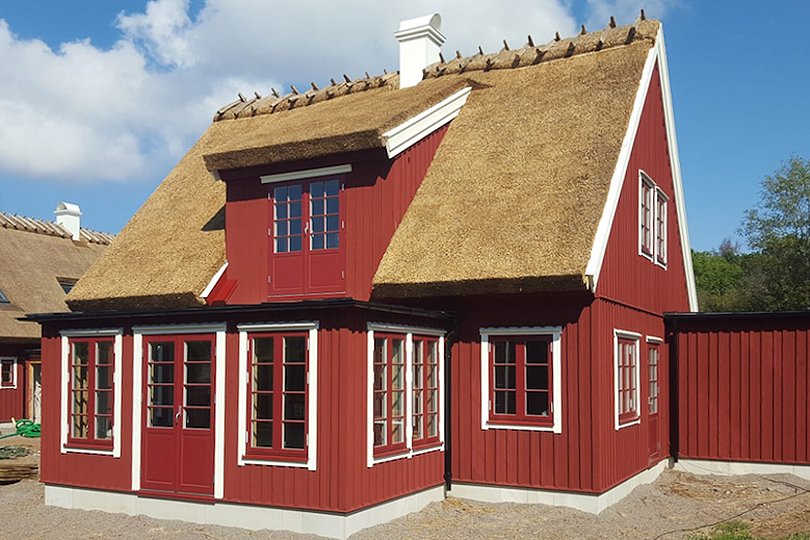 rött träbyggnad med halmtak och träfönster med sprosser
